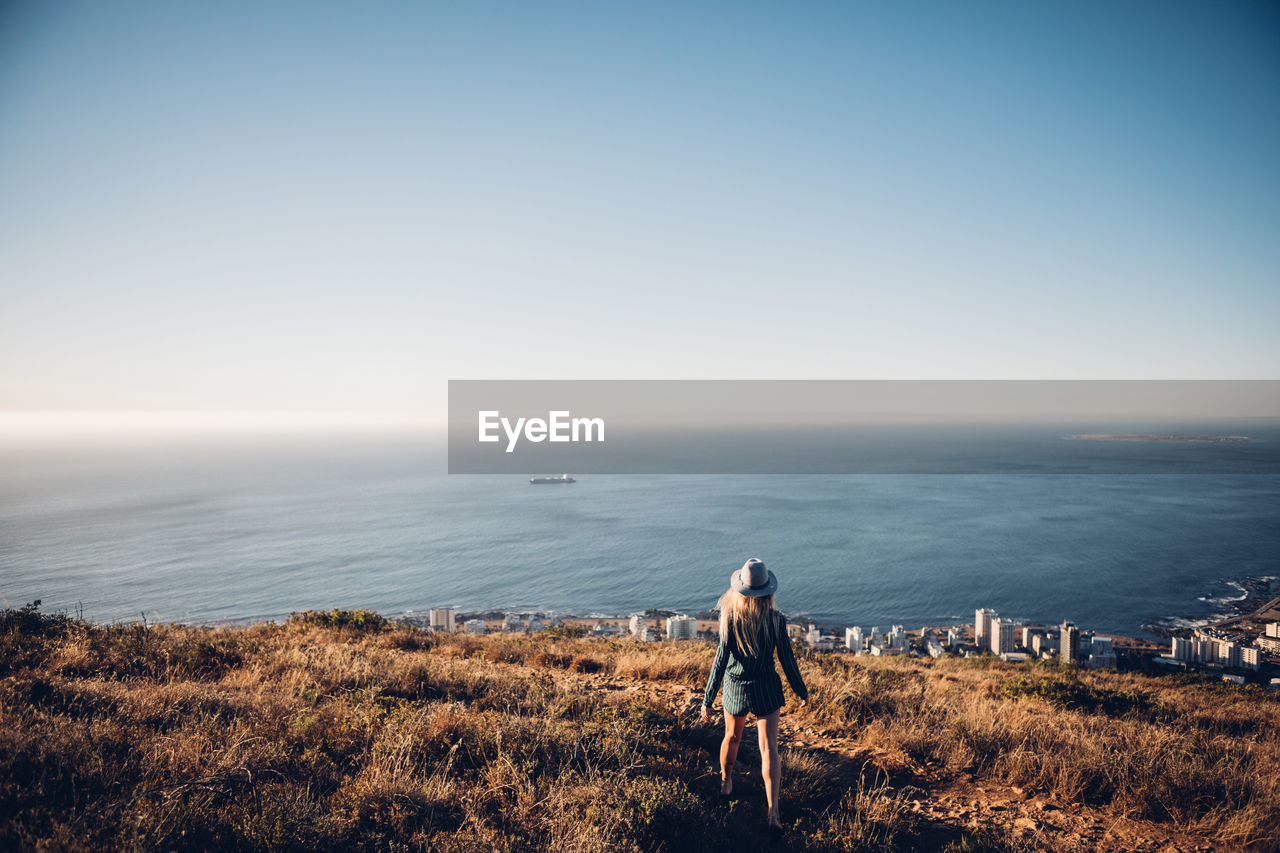 Rear view of woman standing on shore at beach against clear sky