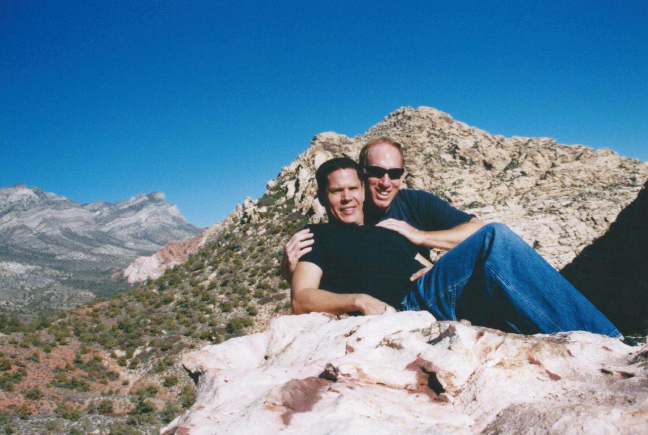 Portrait of father and son resting on rocky mountain against clear blue sky