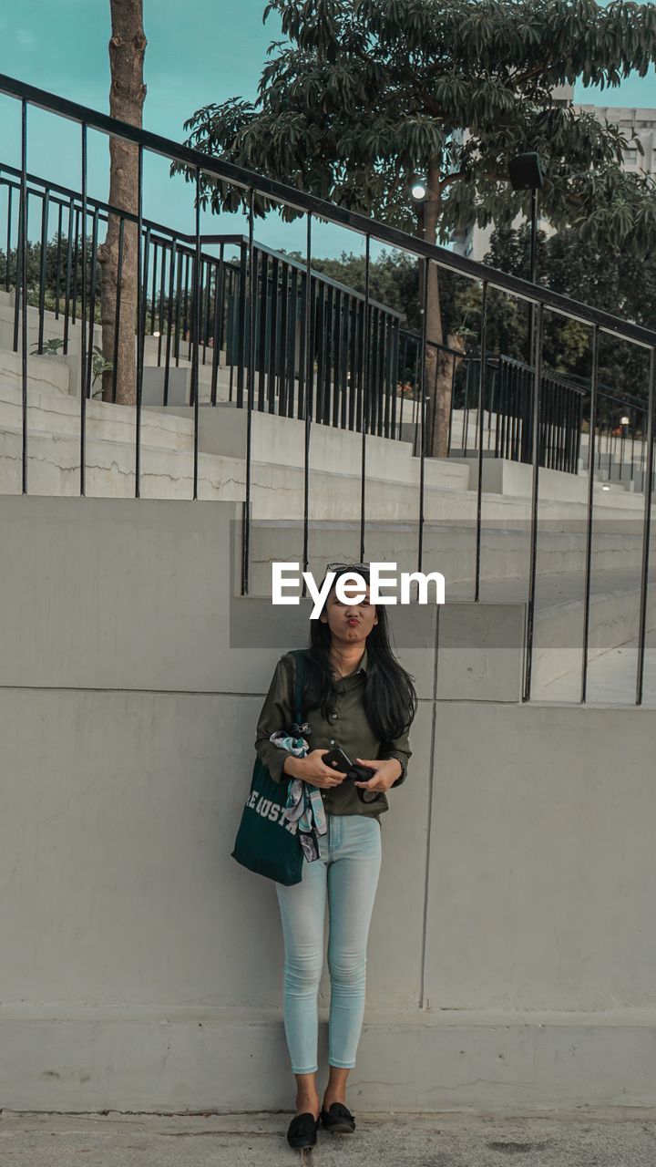 Portrait of young woman standing against railing