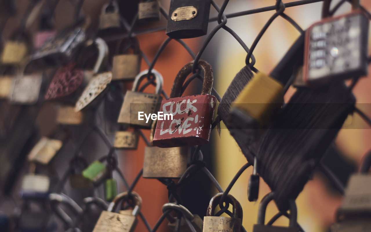 CLOSE-UP OF LOVE PADLOCKS HANGING ON METAL CHAIN