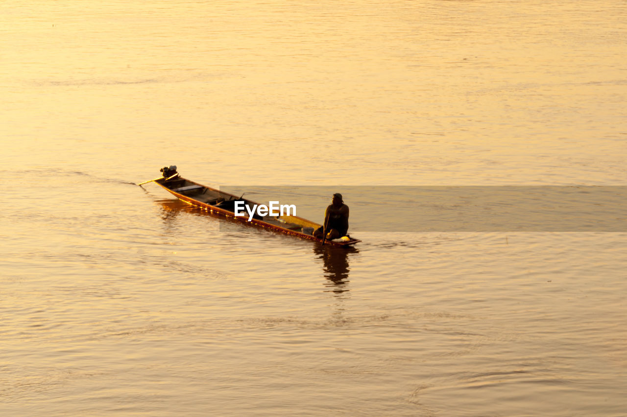 Fisherman in boat on sea during sunset