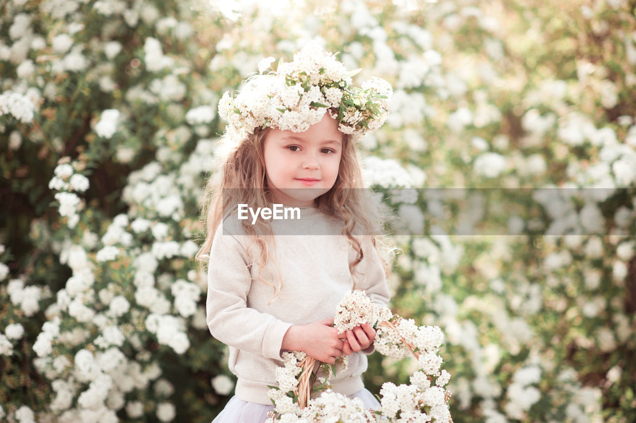 flower, flowering plant, plant, women, spring, one person, bride, nature, dress, portrait, child, hairstyle, childhood, clothing, beauty in nature, long hair, happiness, smiling, fashion, wreath, emotion, female, blond hair, adult, freshness, blossom, wedding dress, white, front view, innocence, pink, looking at camera, outdoors, portrait photography, crown, laurel wreath, celebration, looking, flower arrangement, springtime, day, young adult, royalty, tree, standing, bouquet, three quarter length, event, lifestyles, cute, person, positive emotion, wedding, waist up