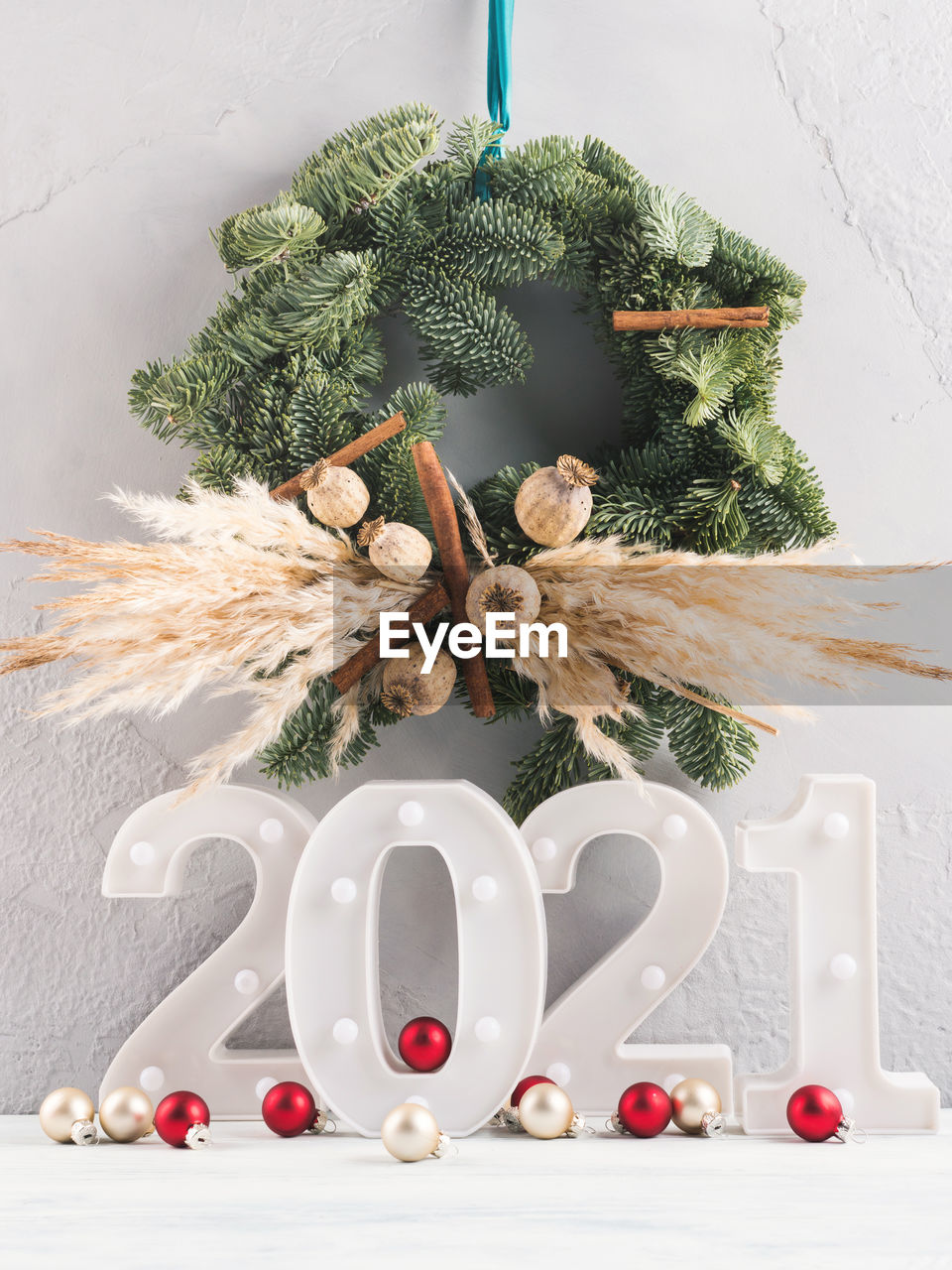 New 2021 year numbers lights with festive xmas red decor, spruce wreath on gray wall 