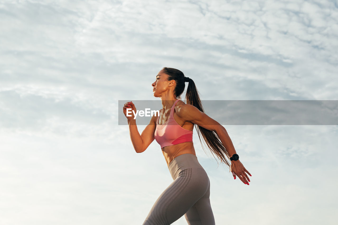 side view of young woman exercising against sky