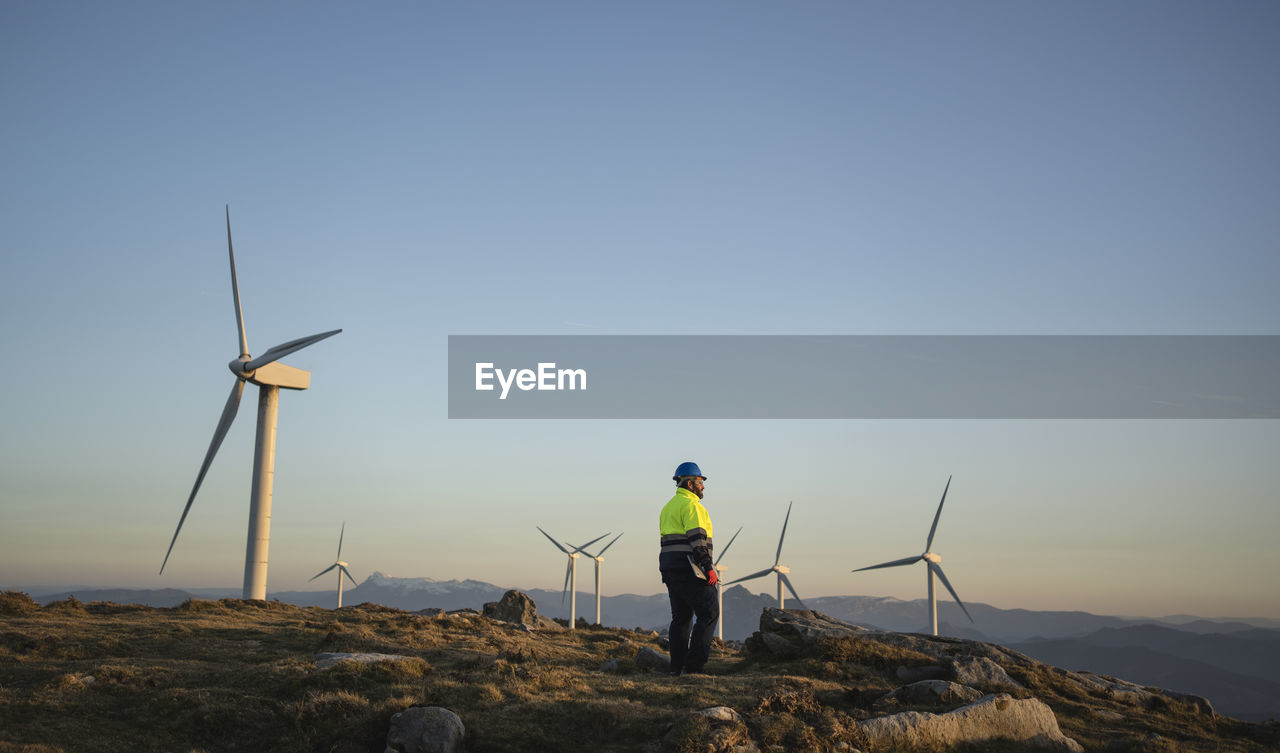 Engineer looking at sunset standing amidst wind turbines