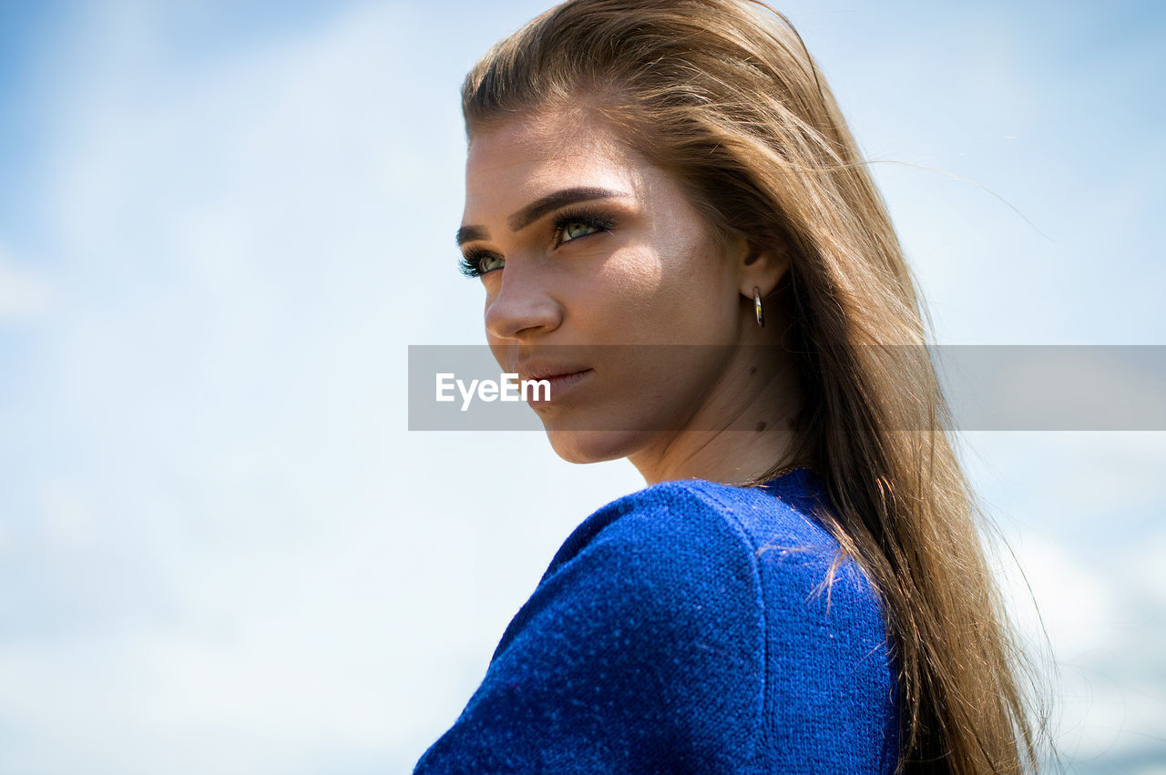 Young woman looking away against sky