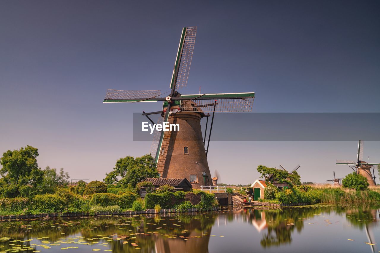 Traditional windmill by lake against clear sky