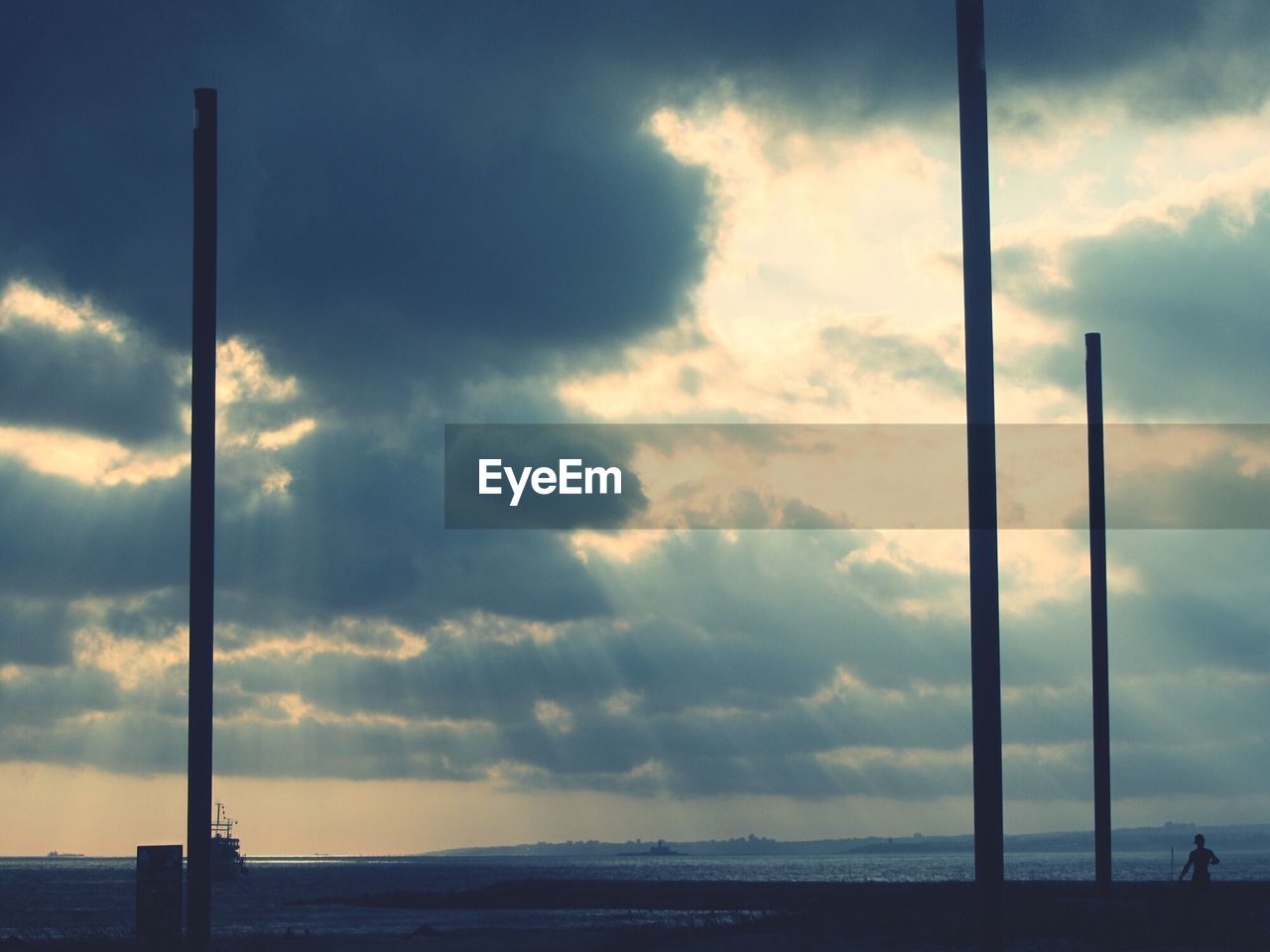 Silhouette poles at sea shore against cloudy sky