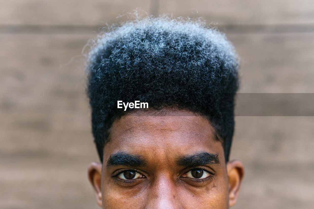 Crop determined african american male with dyed curly hair standing in city and looking at camera