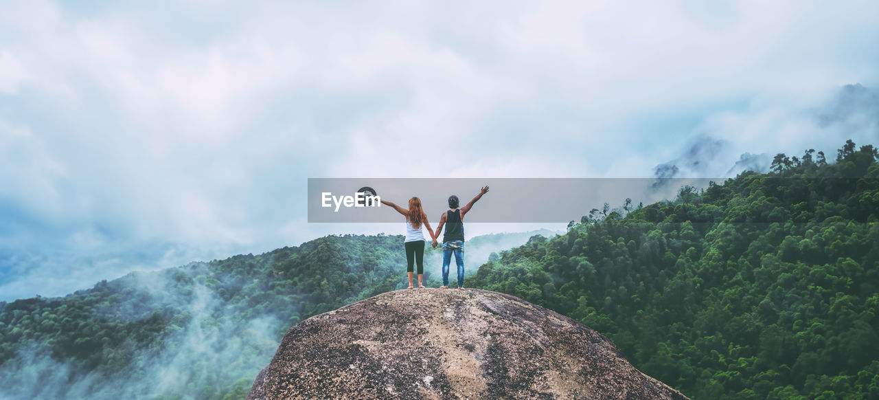 mountain, arm, adult, sky, nature, rock, cloud, limb, leisure activity, adventure, environment, arms raised, beauty in nature, scenics - nature, vacation, trip, activity, human limb, full length, one person, holiday, travel, men, arms outstretched, young adult, land, landscape, outdoors, day, mountain range, hiking, standing, lifestyles, women, sports, mountain peak, success, travel destinations, person, tranquility, emotion, achievement, happiness, forest, communication, vitality, tree, extreme sports, rear view, copy space, plant, motion, cliff, sea