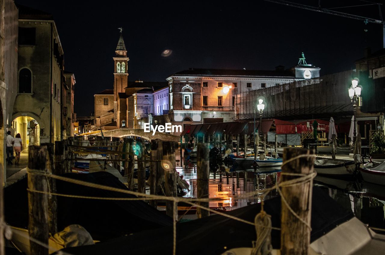 Boats moored at canal against buildings in city at night