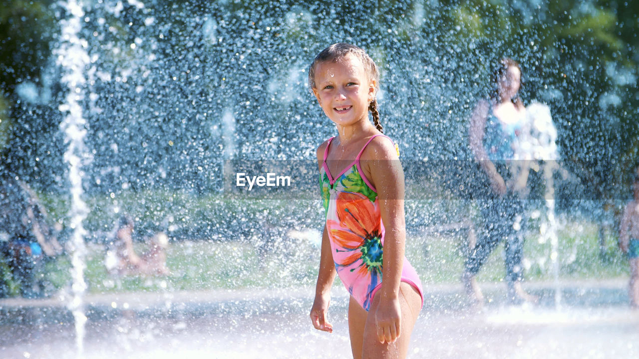 Happy girl of seven years, in swimsuit, having fun between water splashes in fountain . sunny