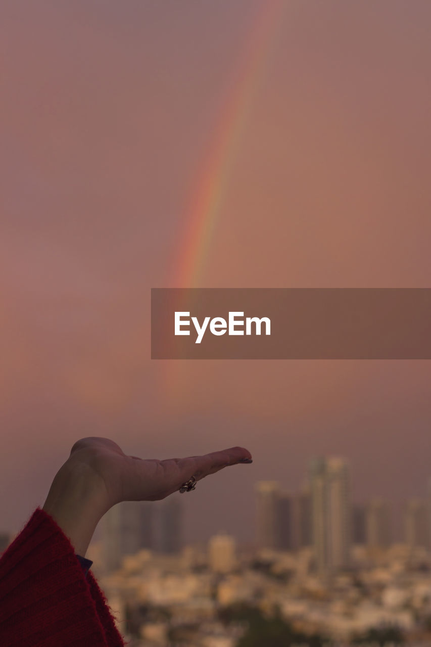 Close-up of hand against rainbow in sky