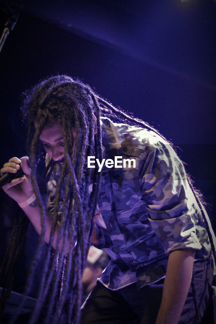 Low angle view of young man with dreadlocks singing on stage