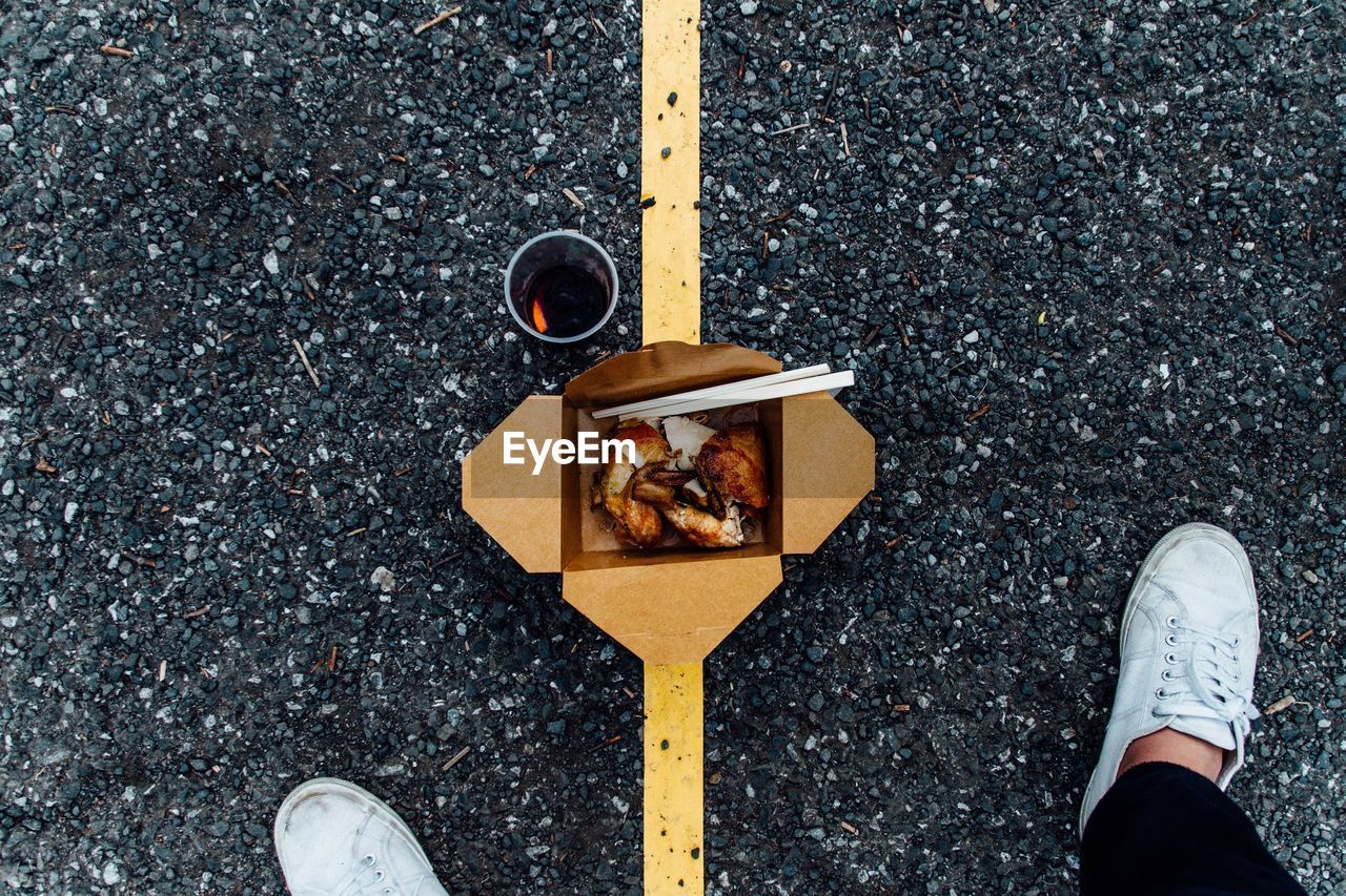 Low section of man standing by take out food with drink on gravel