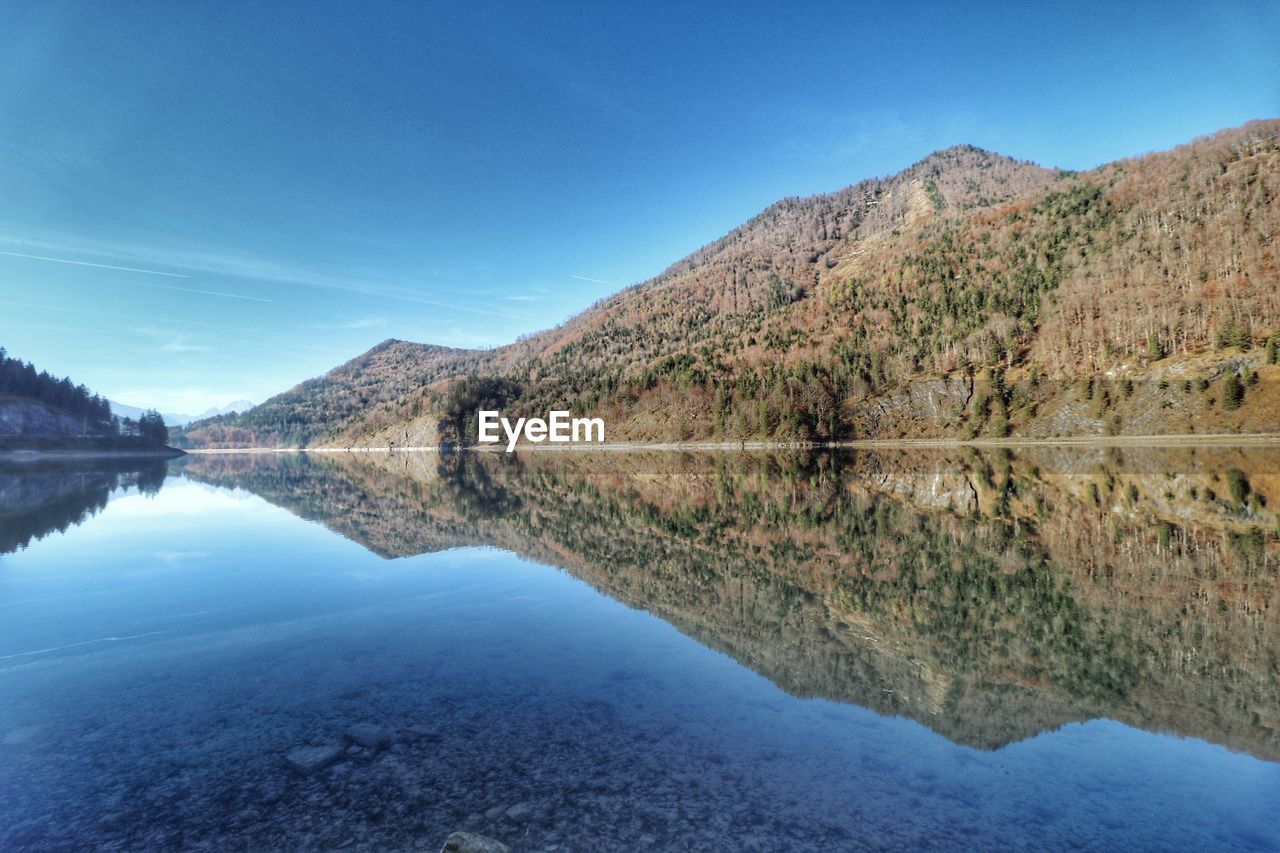water, reflection, mountain, scenics - nature, lake, sky, beauty in nature, nature, reservoir, landscape, environment, tranquility, tranquil scene, blue, no people, mountain range, land, body of water, wilderness, tree, travel destinations, plant, non-urban scene, outdoors, clear sky, day, travel, morning, idyllic