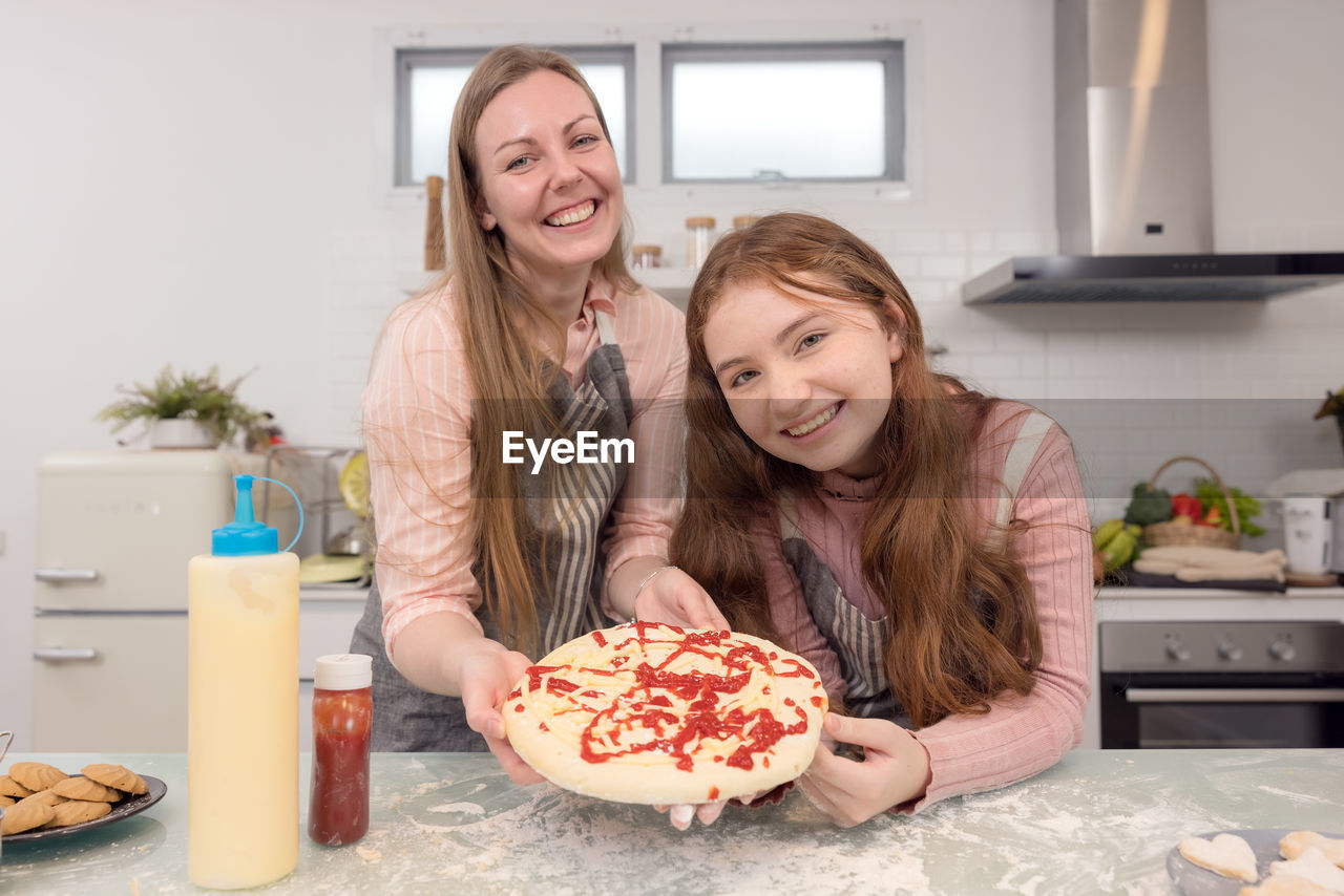 In the kitchen at home, a playful mother and daughter yell while making pizza dough.