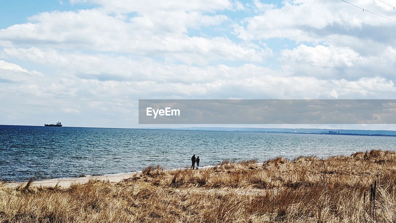 water, sky, sea, shore, horizon, land, cloud, beach, body of water, nature, scenics - nature, beauty in nature, coast, ocean, horizon over water, tranquility, sand, day, tranquil scene, holiday, vacation, trip, one person, leisure activity, cliff, outdoors, non-urban scene, bay, men, wave, idyllic, standing, travel, adult, landscape, lifestyles, travel destinations, rock, environment, blue, rear view, full length