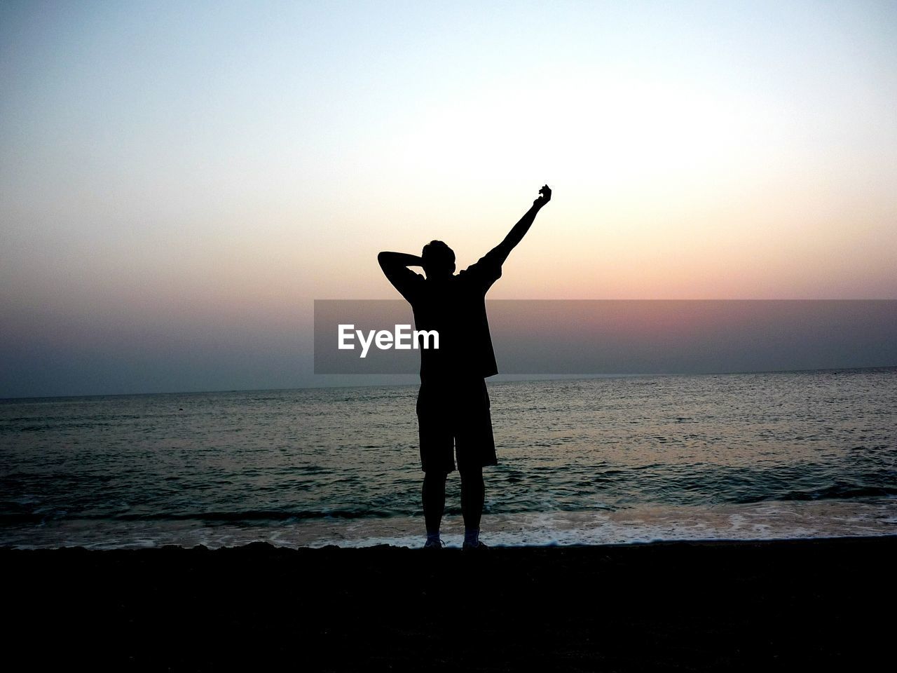 Silhouette man standing on shore at beach against sky during sunset