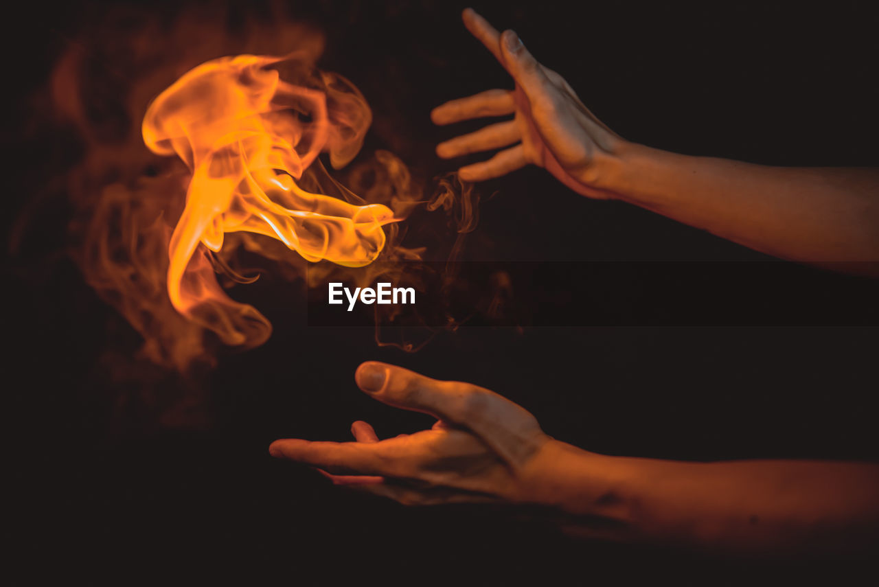 Cropped hands of person by flame against black background