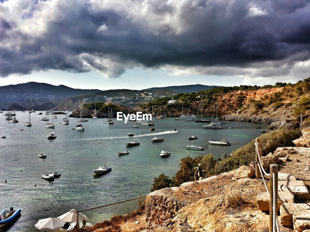 Sailboats moored on sea by mountains against cloudy sky