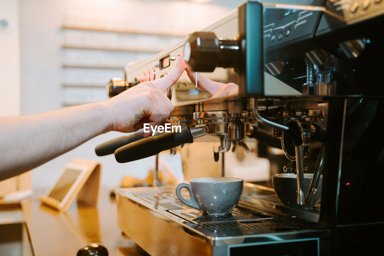 Unrecognizable crop barista preparing hot drink in modern coffee machine while working in cafe