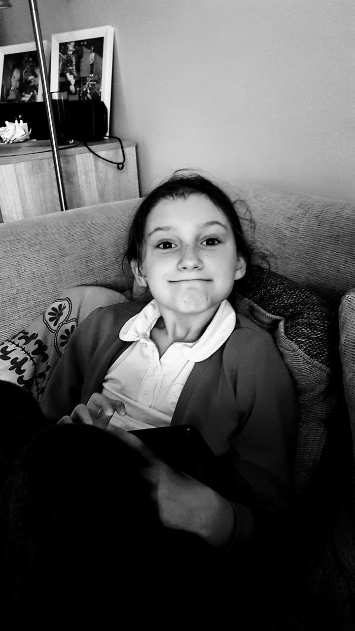 PORTRAIT OF HAPPY GIRL SITTING ON SOFA AT HOME