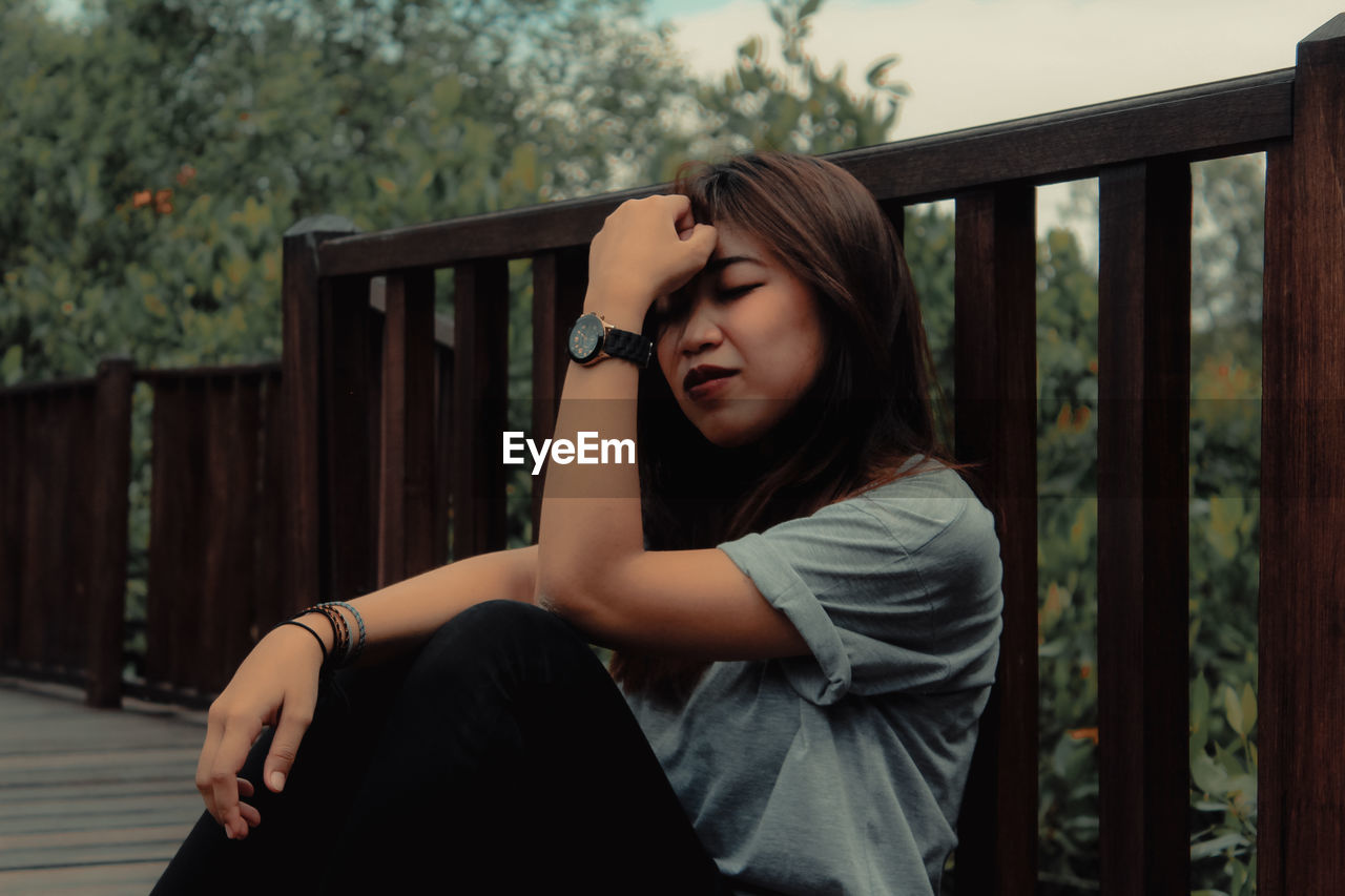 Young woman sitting against railing and trees