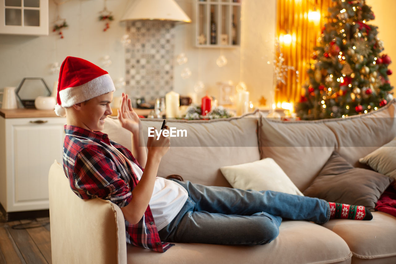 Teenage boy in santa's hat sits in a christmas-decorated room and chats online. 