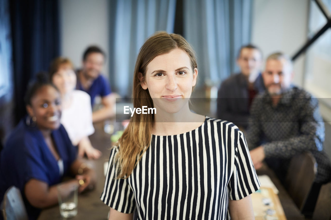 Portrait of confident businesswoman standing while colleagues in background at office