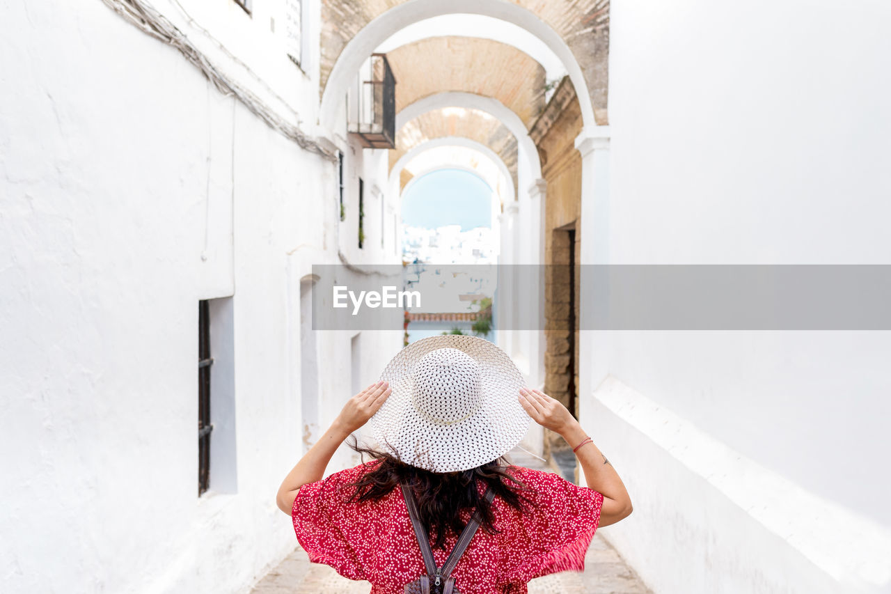 Back view of unrecognizable female tourist with raised arms on narrow street between old houses in greece
