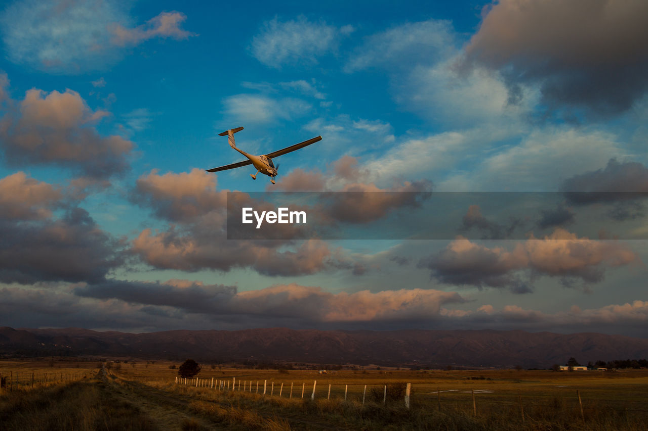 LOW ANGLE VIEW OF AIRPLANE FLYING OVER FIELD