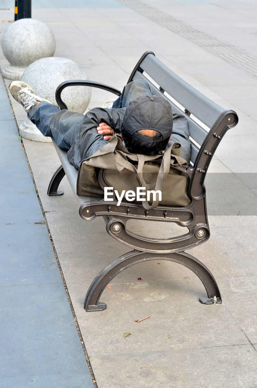 Full length of man lying on bench at sidewalk