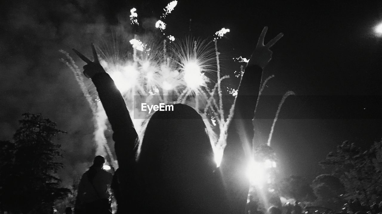 Rear view of woman with peace sign against firework display at night