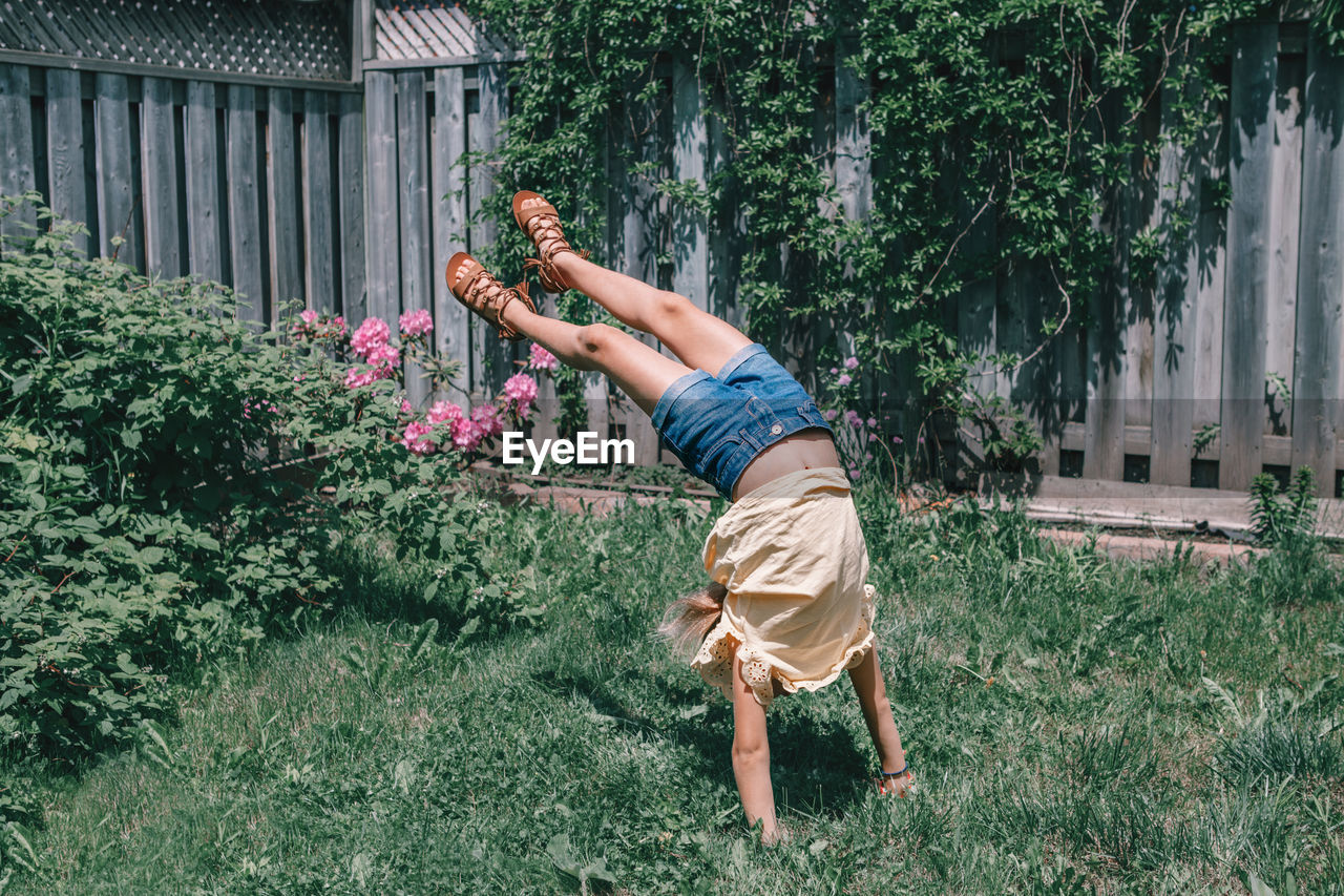 Girl balancing on handstand at yard against fence