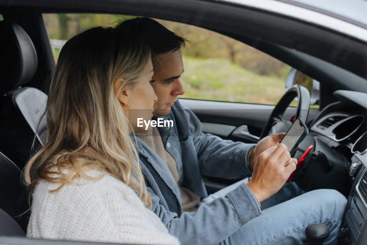 A young couple on a road trip looking at a map on their phone in a navigator.