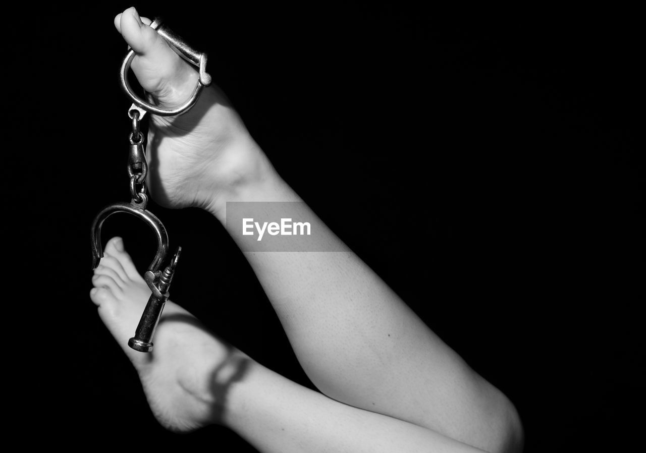 Low section of woman with handcuffs against black background