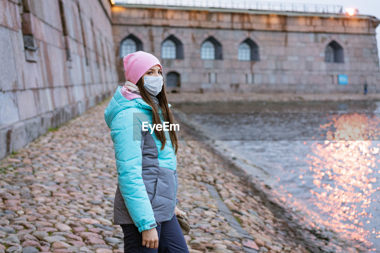 A woman walks in the city by the river in a protective mask