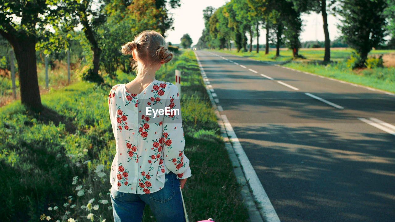 Rear view of woman standing on road against trees