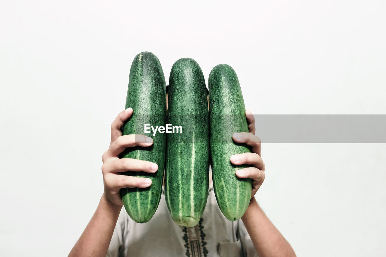 Woman holding cucumber against white background