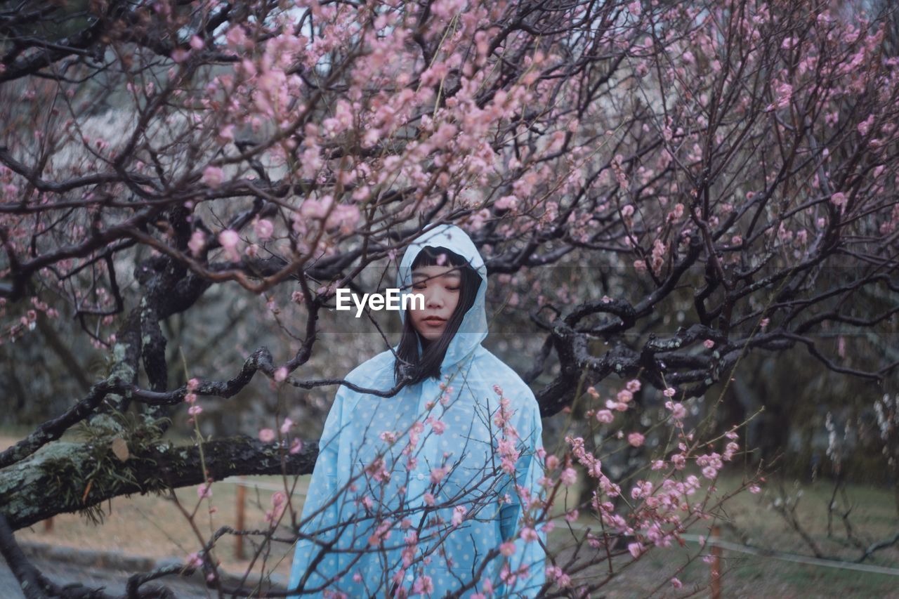 YOUNG WOMAN WITH PINK FLOWERS STANDING ON TREE