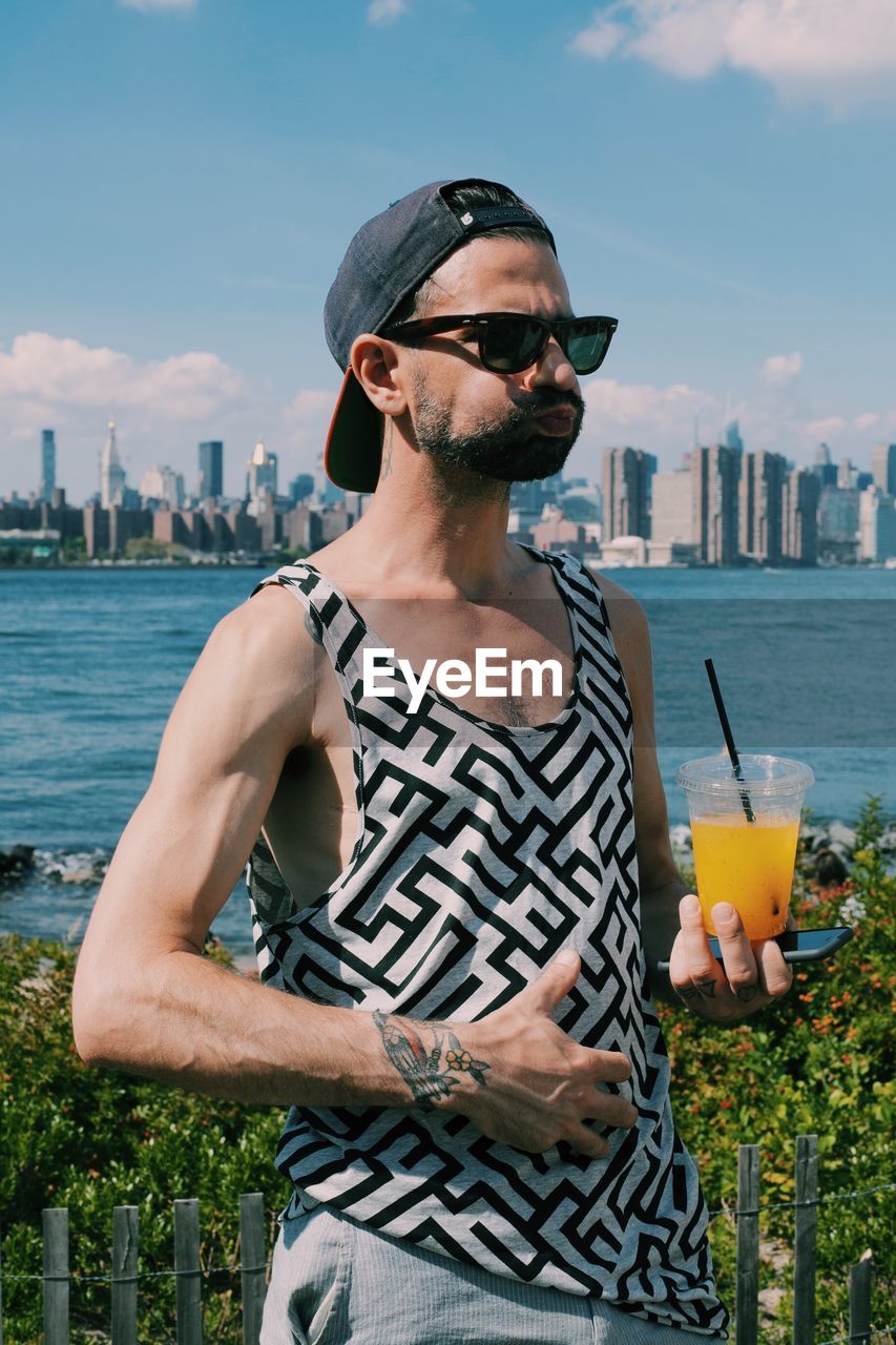 Man drinking juice while standing against sea and sky in city