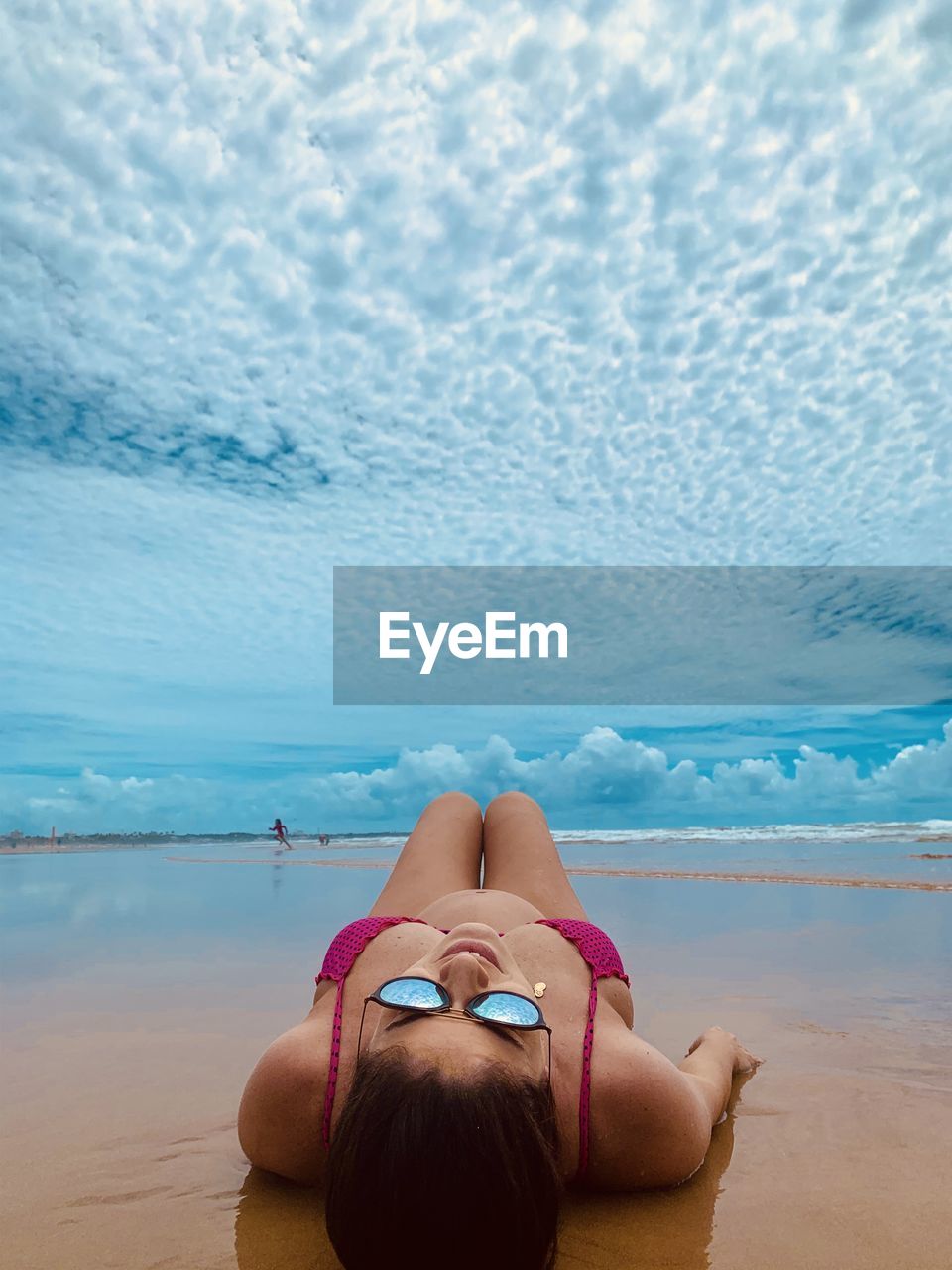  woman wearing sunglasses lying down on beach against dramatic sky