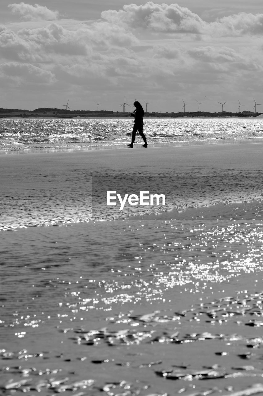 SILHOUETTE OF PERSON ON BEACH AGAINST SKY