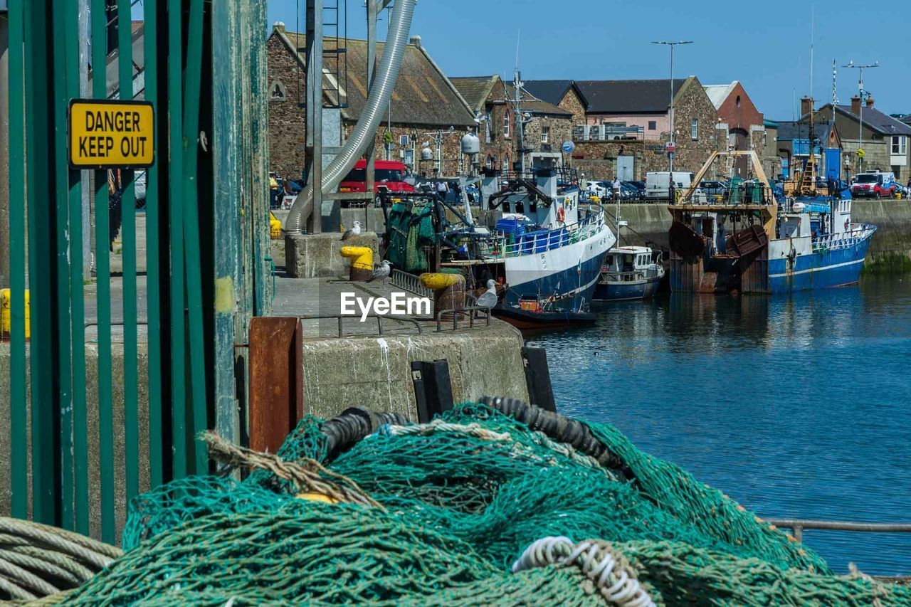 FISHING BOATS MOORED AT HARBOR AGAINST SEA