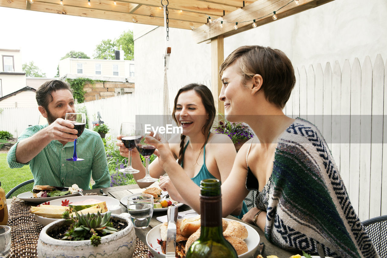 Friends toasting wineglasses while sitting at table in yard