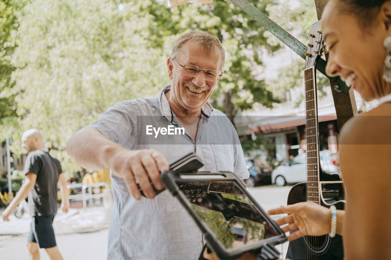 Happy senior male customer paying through contactless payment while shopping at flea market