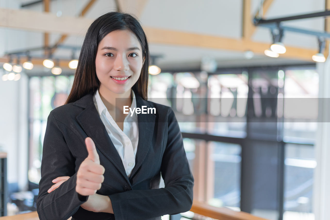 Portrait of confident businesswoman gesturing thumbs up in office
