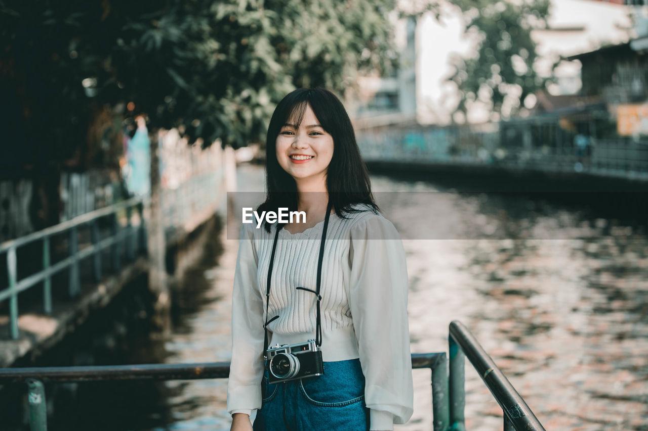 Portrait of smiling young woman standing by railing