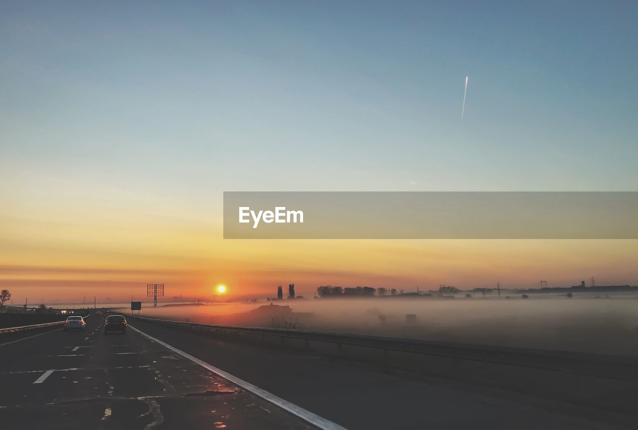 Road by city against sky during sunset